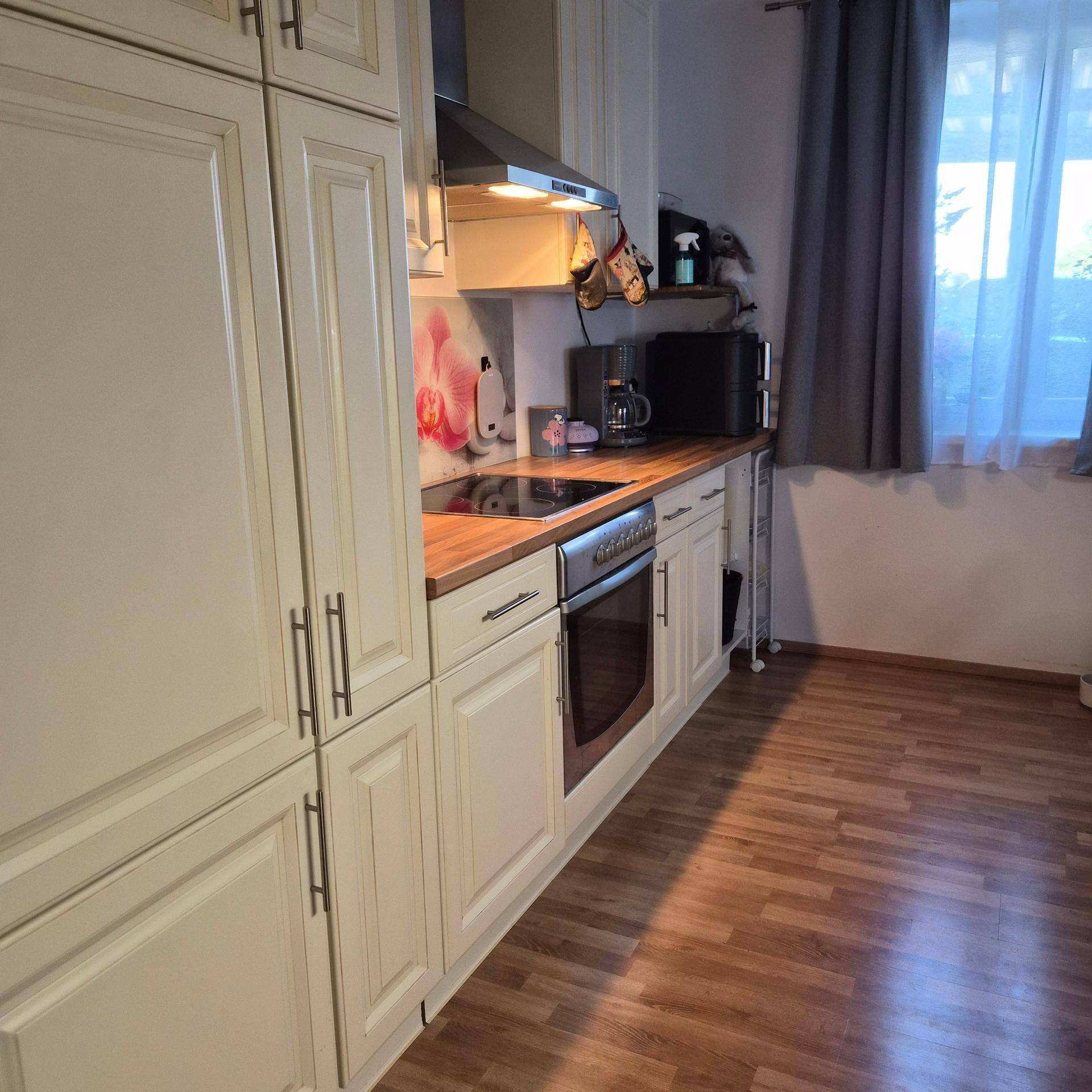 Funktionale Küche mit weißen Schränken, Holzarbeitsplatte, eingebautem Backofen und Induktionskochfeld.