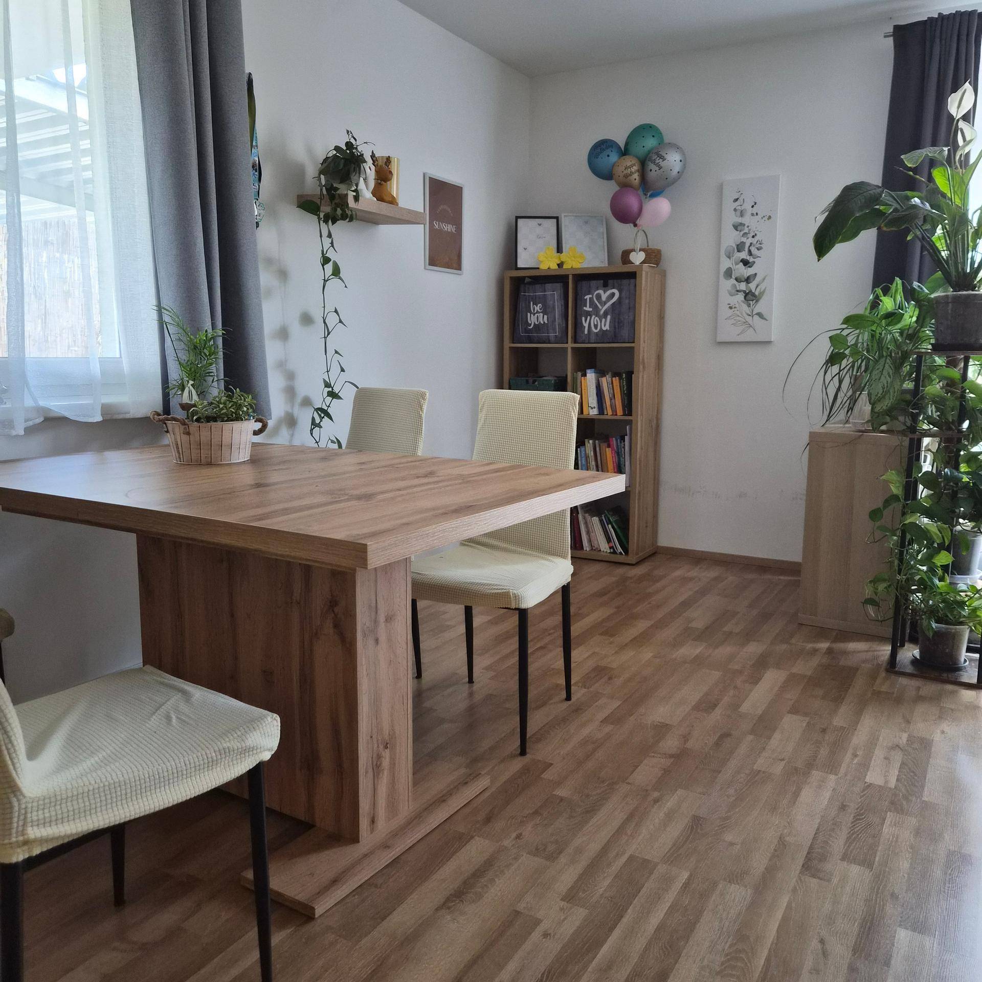 Heller Essbereich mit Holztisch und Stühlen, umgeben von Pflanzen und natürlichem Licht.