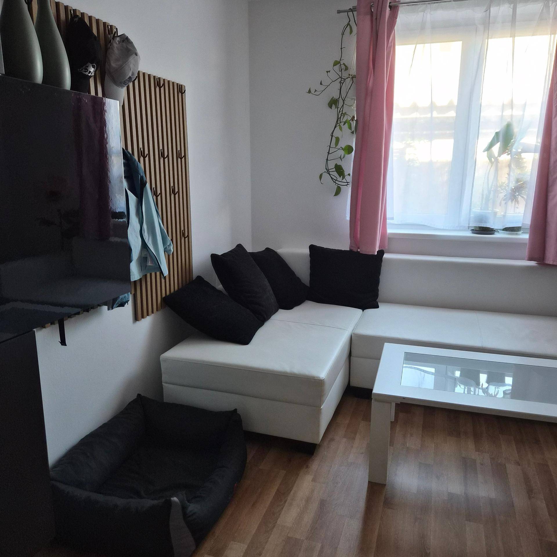 Gemütliche Sitzecke mit weißem Ecksofa, Couchtisch und Holzboden, akzentuiert durch rosa Vorhänge.