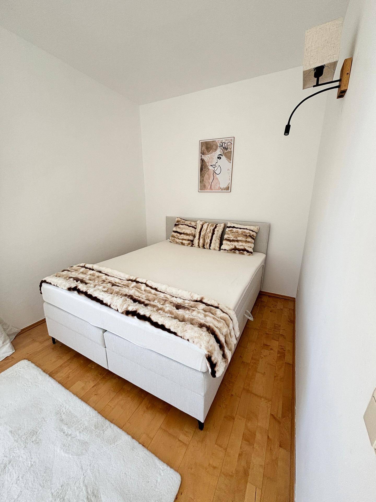 Schlafzimmer mit Doppelbett, hellem Teppich und Wandleuchte in modernem Stil.