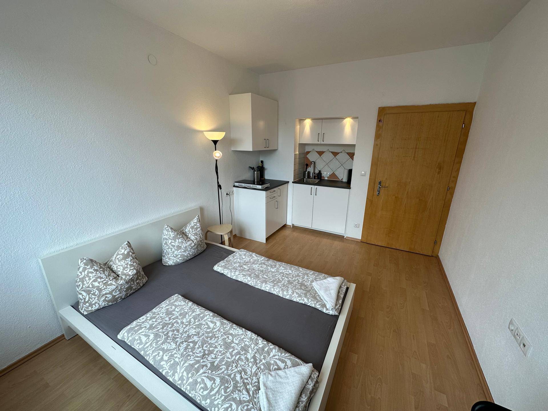 Geräumiges Schlafzimmer mit integrierter Küchenzeile und hellem Holzfußboden.
