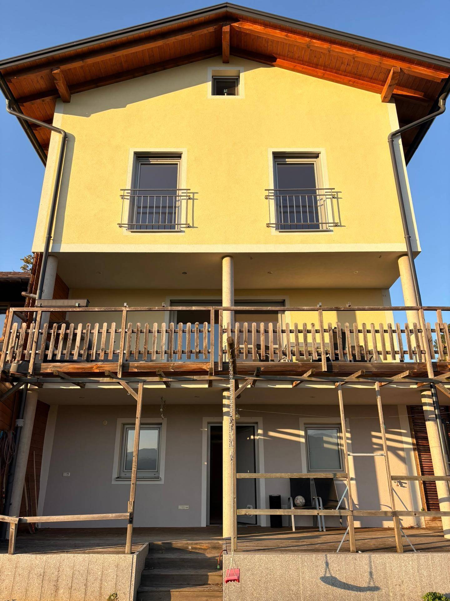 Gelbes Haus mit traditionellen Holzbalkonen und einer überdachten Terrasse im Erdgeschoss.