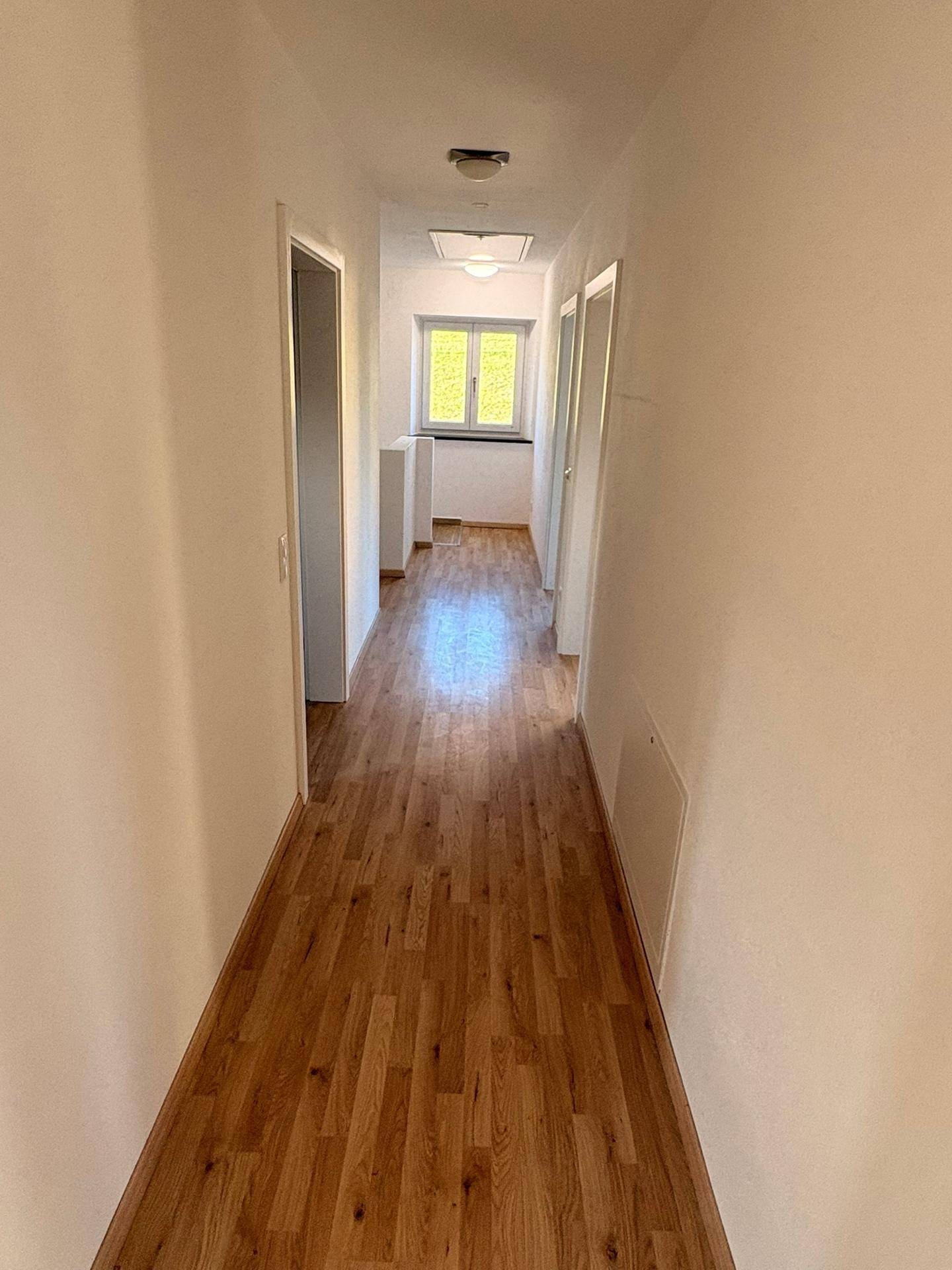 Langer, heller Flur mit Laminatboden und einem Fenster am Ende, das Tageslicht spendet.