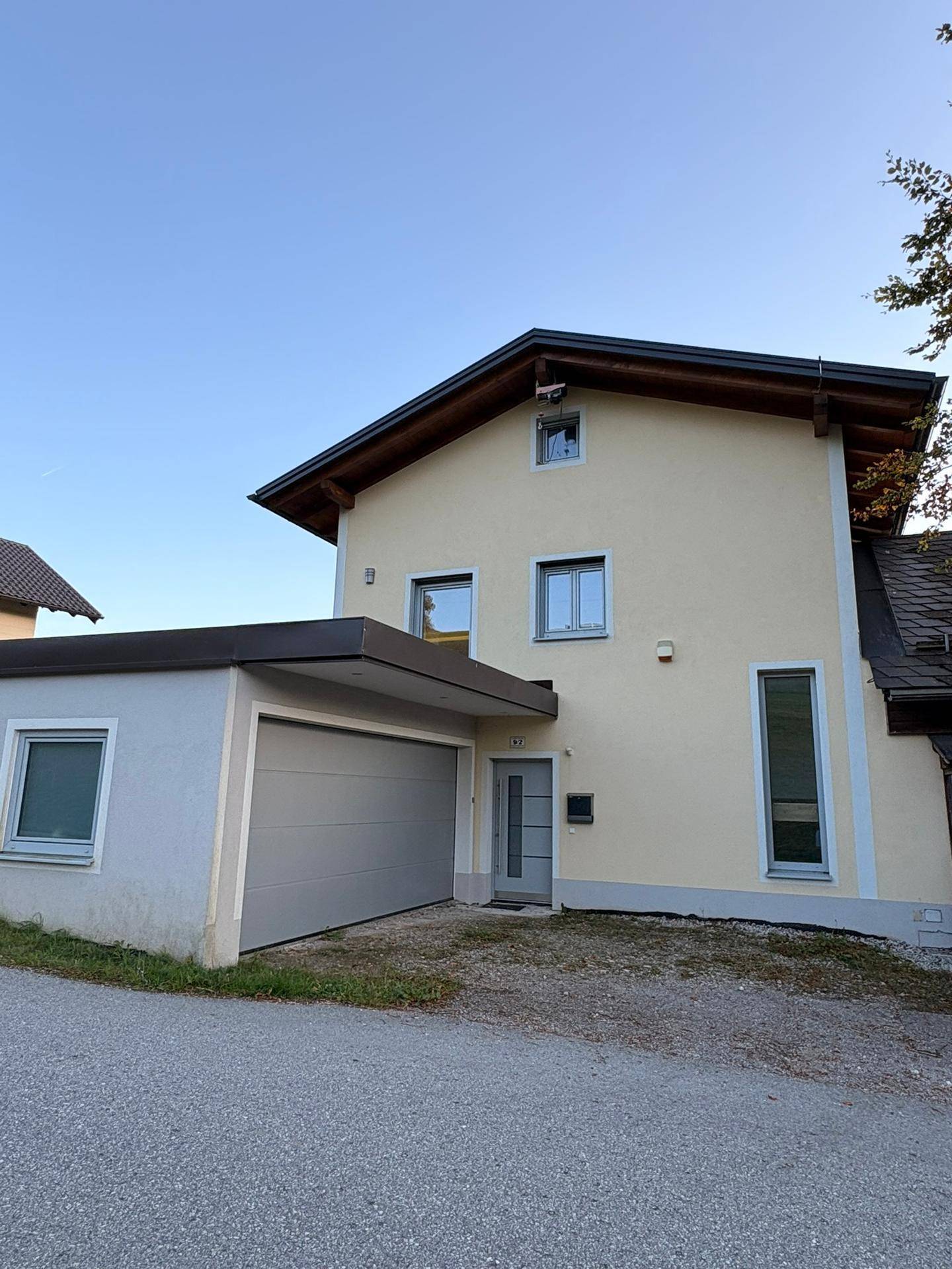 Modernes gelbes Einfamilienhaus mit integrierter Garage und schlichtem Eingangsbereich.