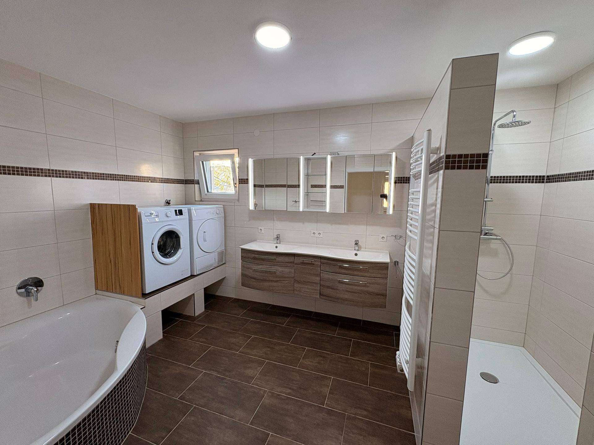 Geräumiges Badezimmer mit Eckbadewanne, Doppelwaschbecken, Dusche und Waschmaschinenanschluss.