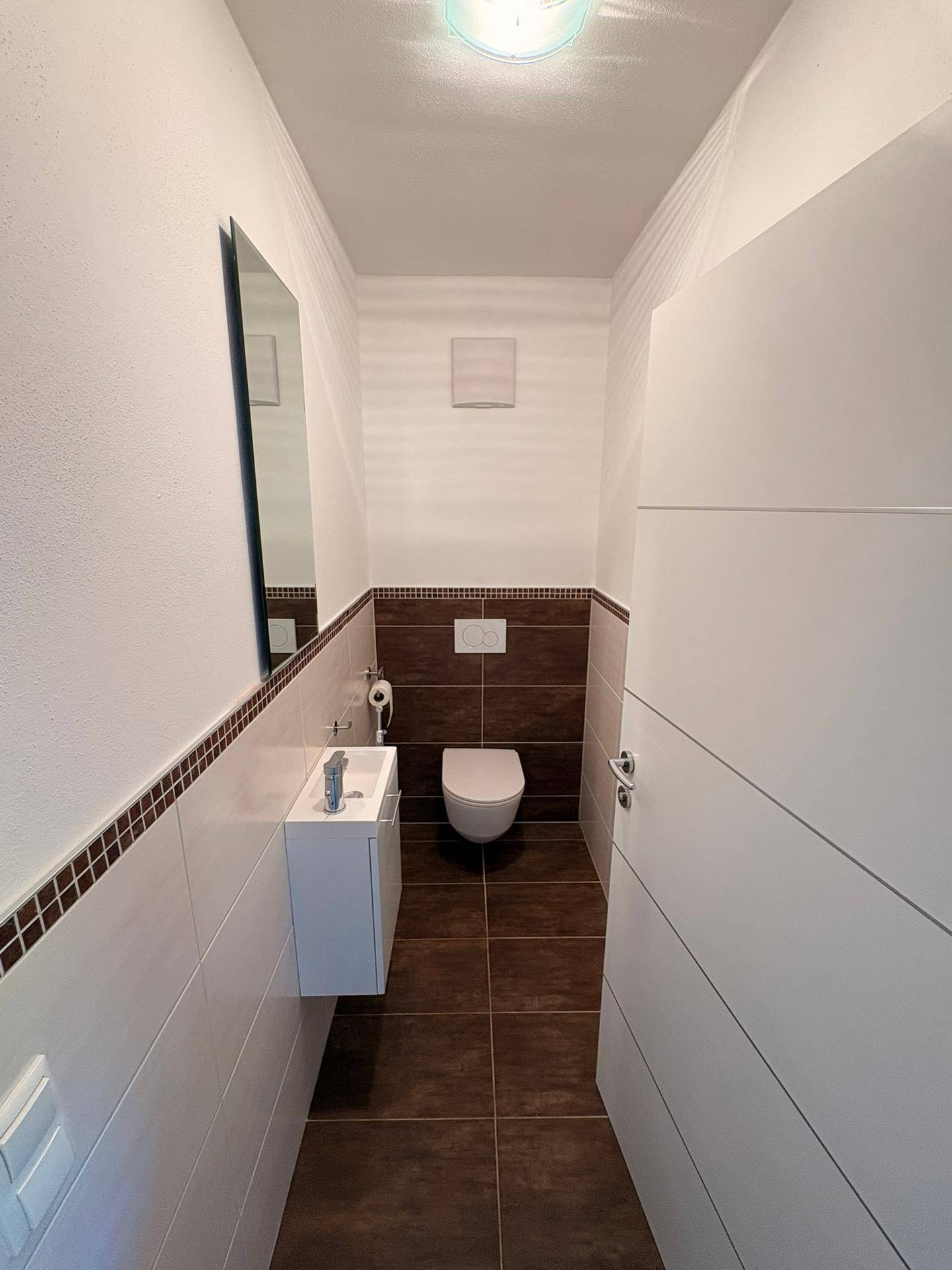 Modernes Gäste-WC mit dunklen Bodenfliesen, wandhängendem WC und kleinem Waschbecken.