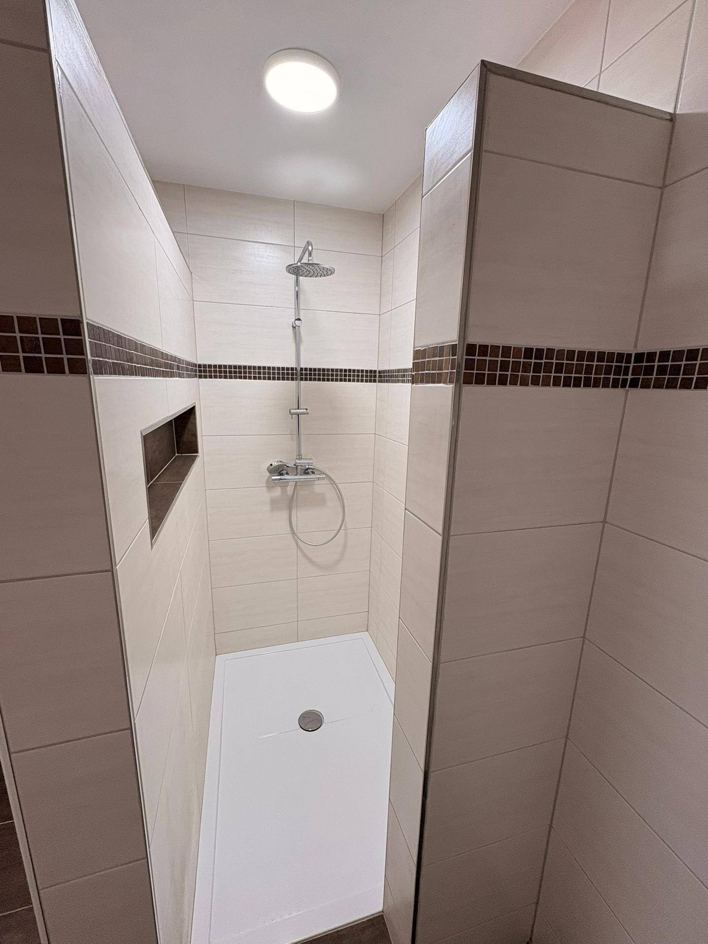 Moderne Duschkabine mit beigen Fliesen, dunklem Akzentstreifen und Regendusche.