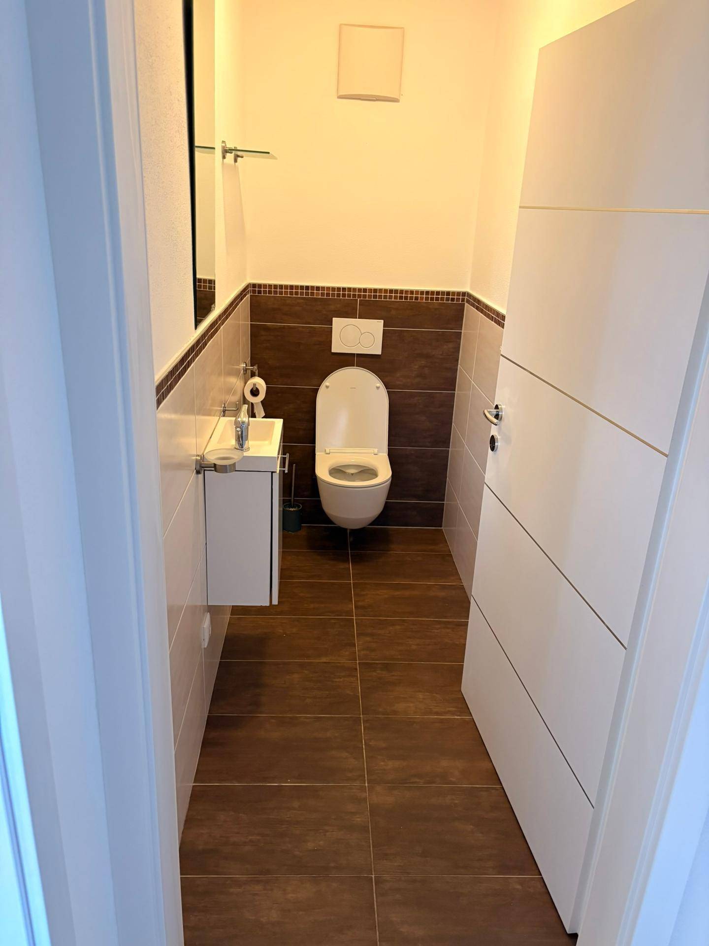 Modernes Gäste-WC mit dunklen Bodenfliesen, wandhängendem WC und kleinem Waschbecken.