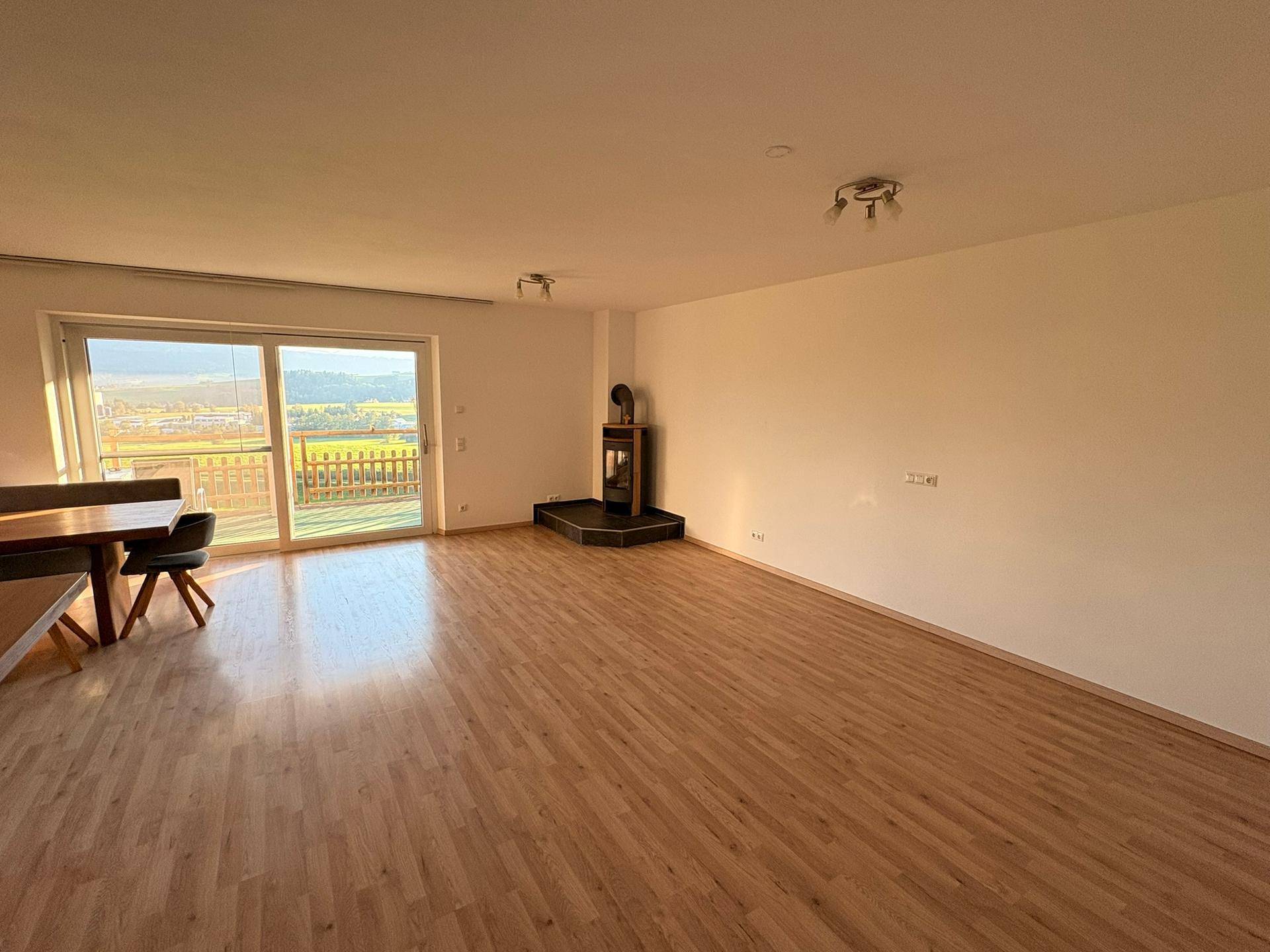 Geräumiger Wohn-Essbereich mit Laminatboden, Kaminofen und großem Schiebefenster zum Außenbereich.