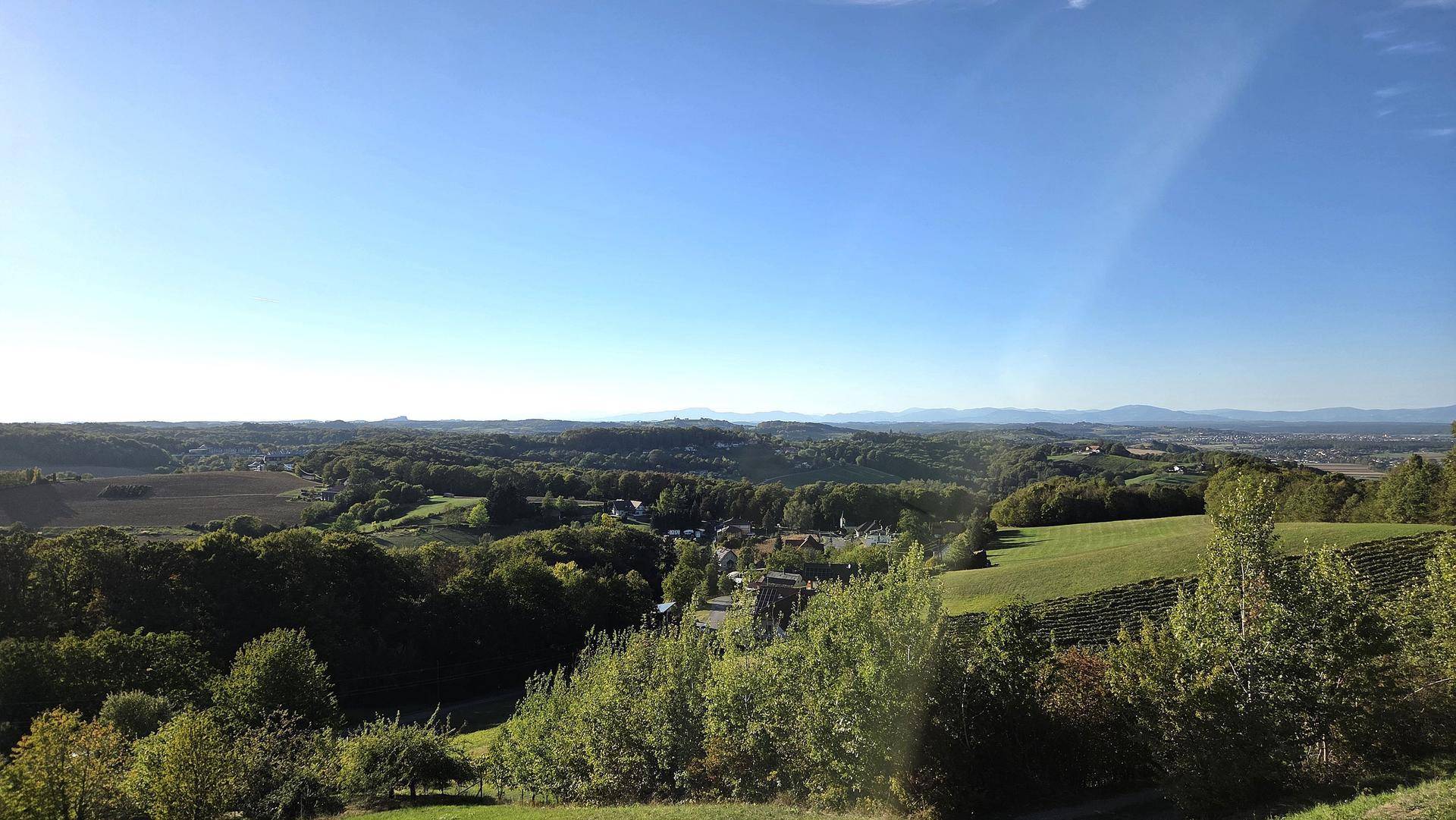 Ruhige Landschaftsaufnahme mit grünen Hügeln, Wäldern und einem weiten Blick in die Ferne.