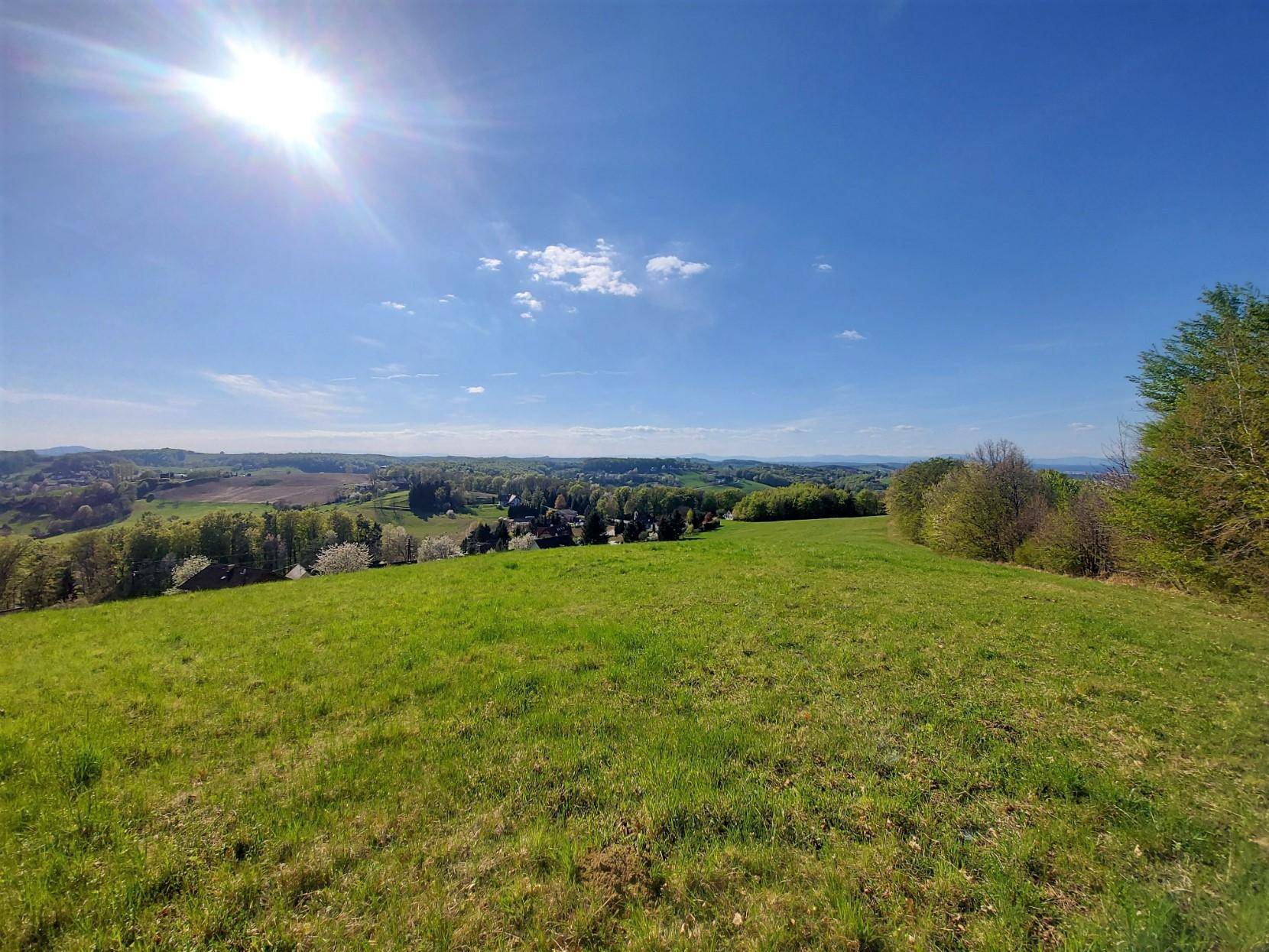 Weite grüne Wiese unter strahlendem Sonnenschein mit Blick auf die umliegende Landschaft.