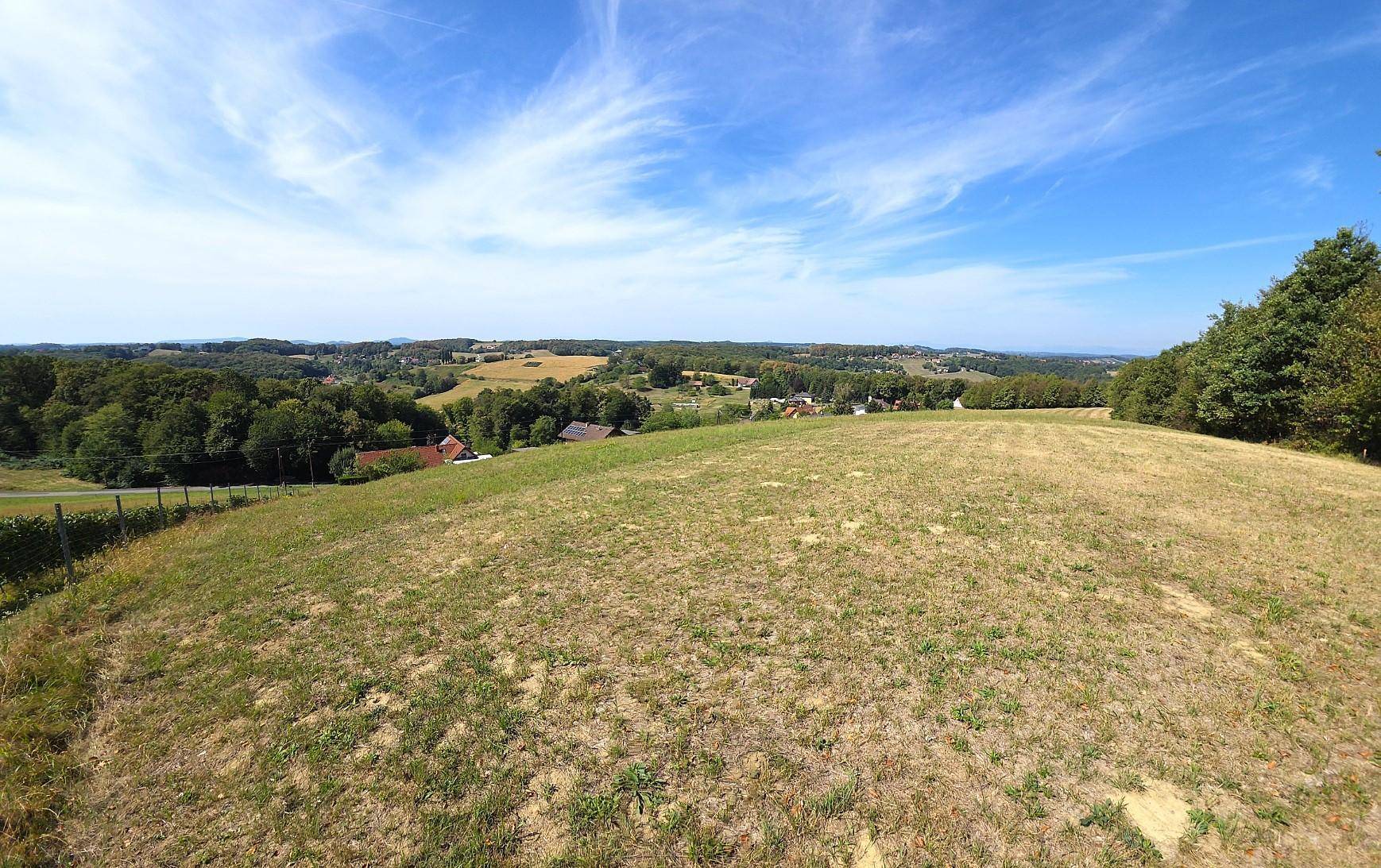 Weitläufige Wiesenlandschaft mit Blick auf die umliegenden Wälder und vereinzelte Gebäude.