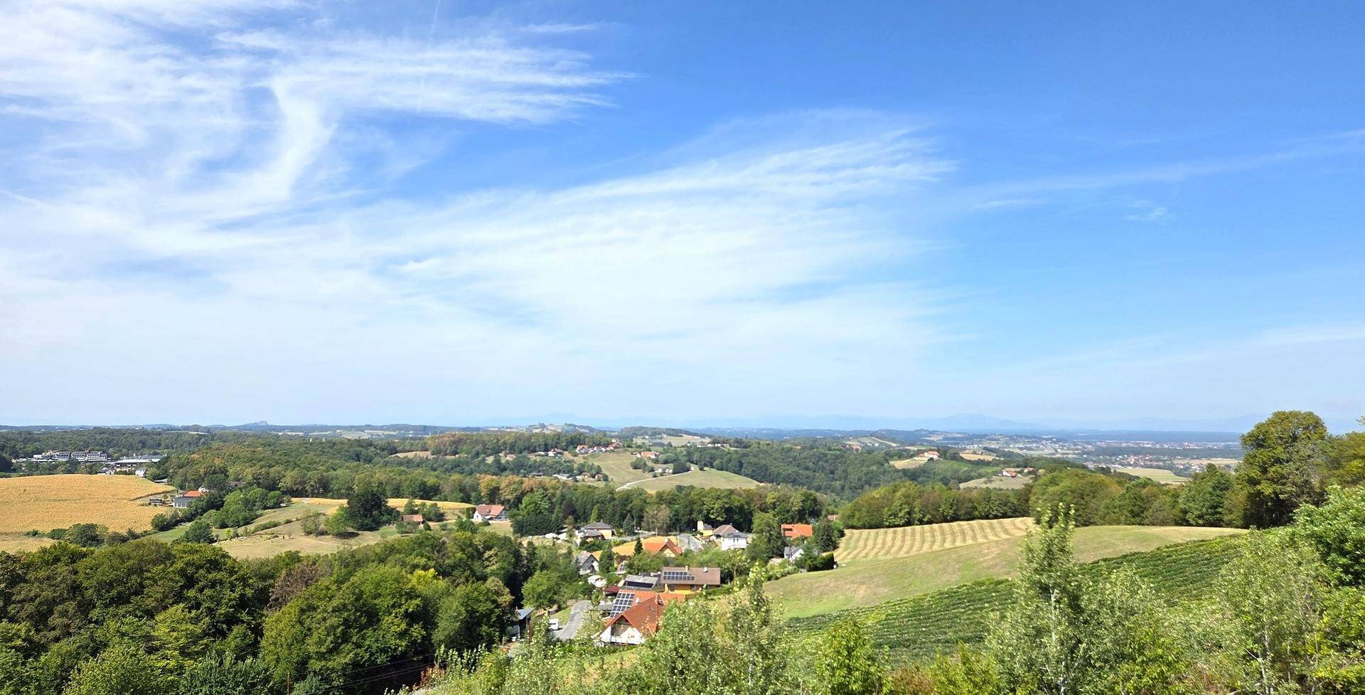 Panoramablick über eine hügelige Landschaft mit Feldern, Weinreben und einem Dorf in der Ferne.