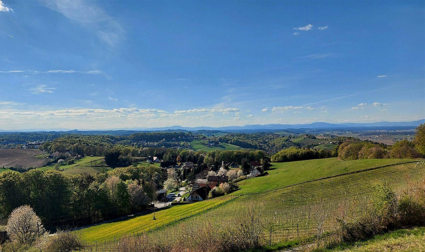 Idyllische Landschaft mit sanften grünen Hügeln, Feldern und einem Dorf in der Ferne.