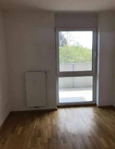 Heller Raum mit Parkettboden und großem Fenster, das viel Tageslicht hereinlässt.