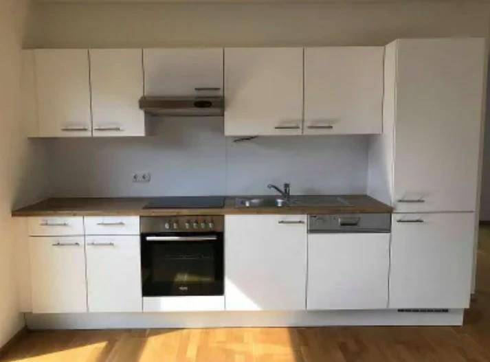 Funktionale Einbauküche mit weißen Schränken, Holz-Arbeitsplatte und integrierten Geräten.