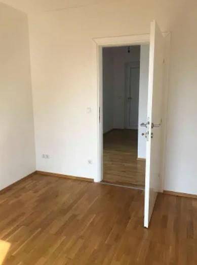Leerer Raum mit Parkettboden und offener Tür, die den Blick in einen weiteren Raum freigibt.