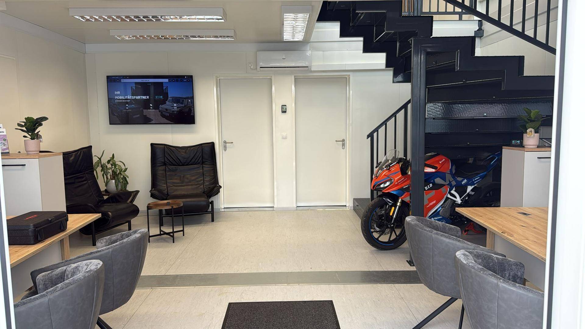 Empfangsbereich mit Treppe, Wartezone, Schreibtischen und einem ausgestellten Motorrad.