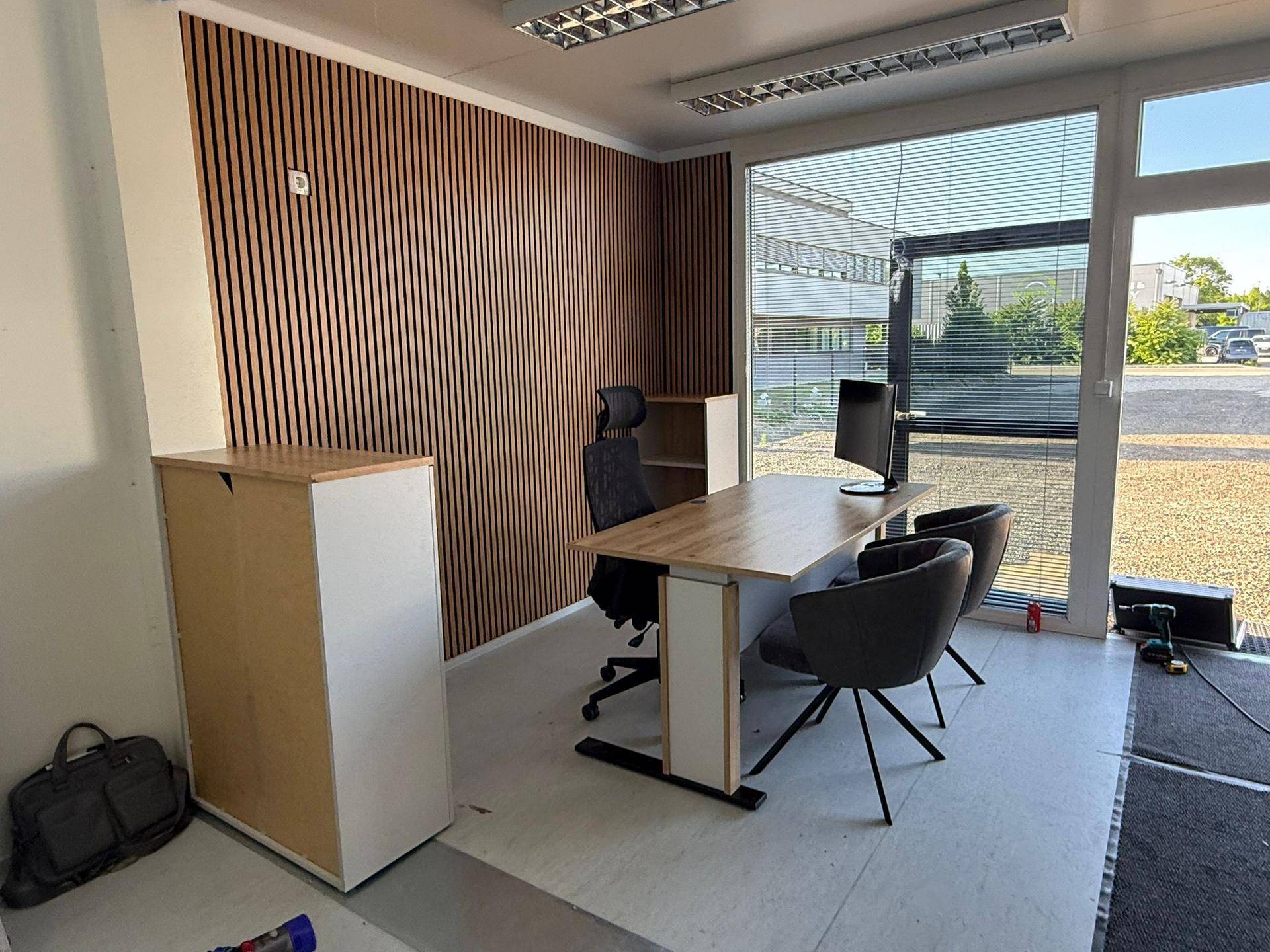 Modernes Büro mit Holzwandverkleidung, Schreibtisch und großem Fenster mit Blick auf den Parkplatz.