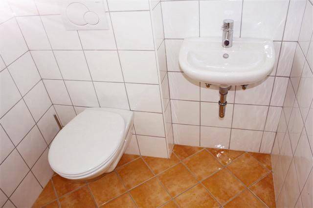 Separates Gäste-WC mit Wand-WC, kleinem Waschbecken und Terrakotta-Fliesenboden.