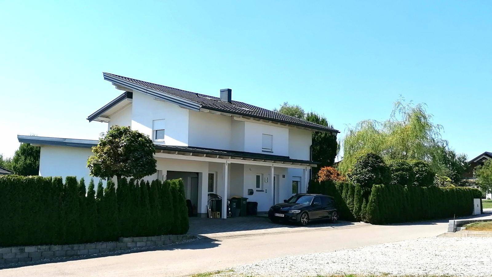 Ansicht des modernen Einfamilienhauses mit Carport, gepflasterter Einfahrt und grüner Hecke.