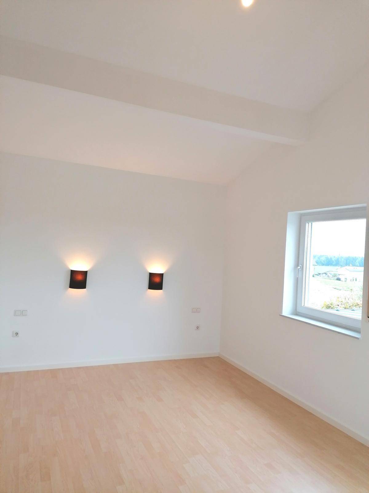 Helles Schlafzimmer mit Laminatboden, schrägen Decken und einem Fenster mit Ausblick.