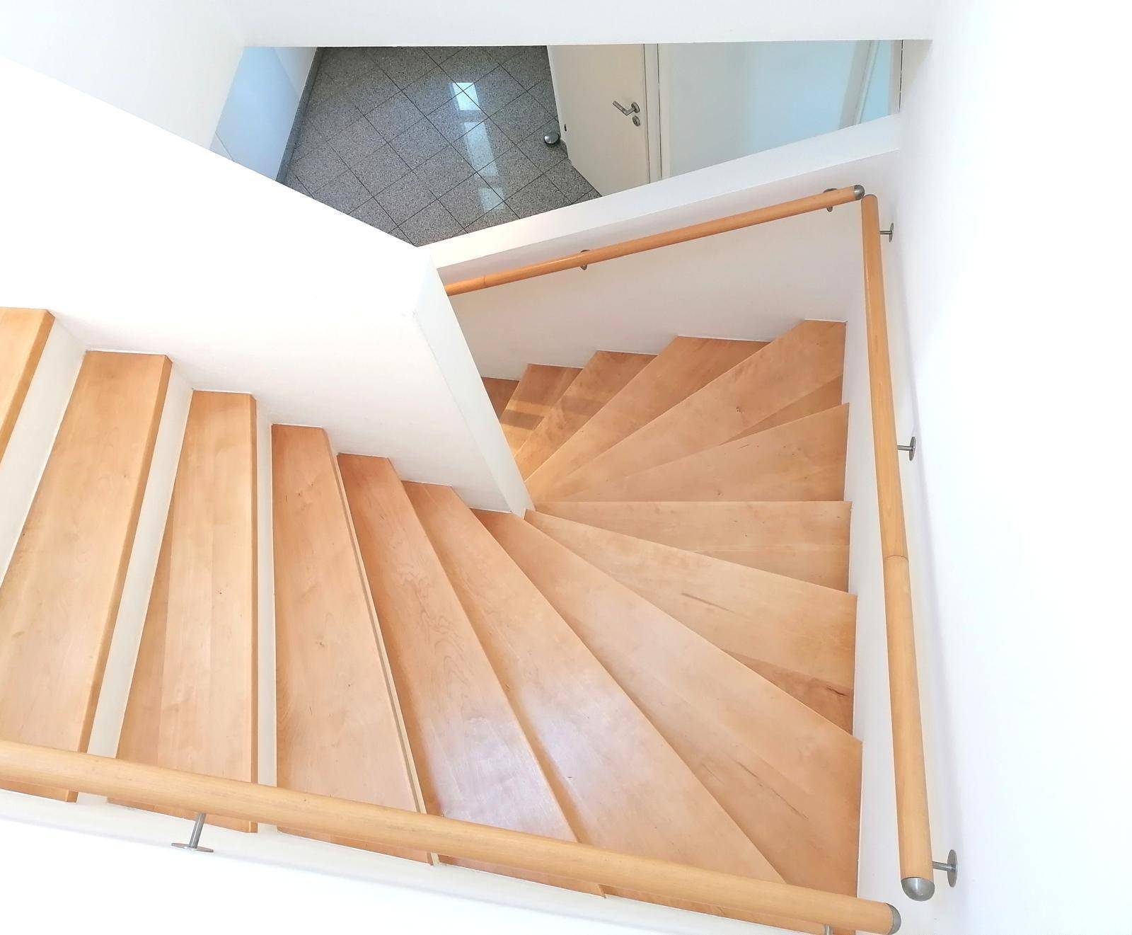 Wendeltreppe aus hellem Holz mit Holzgeländer, die die Stockwerke miteinander verbindet.