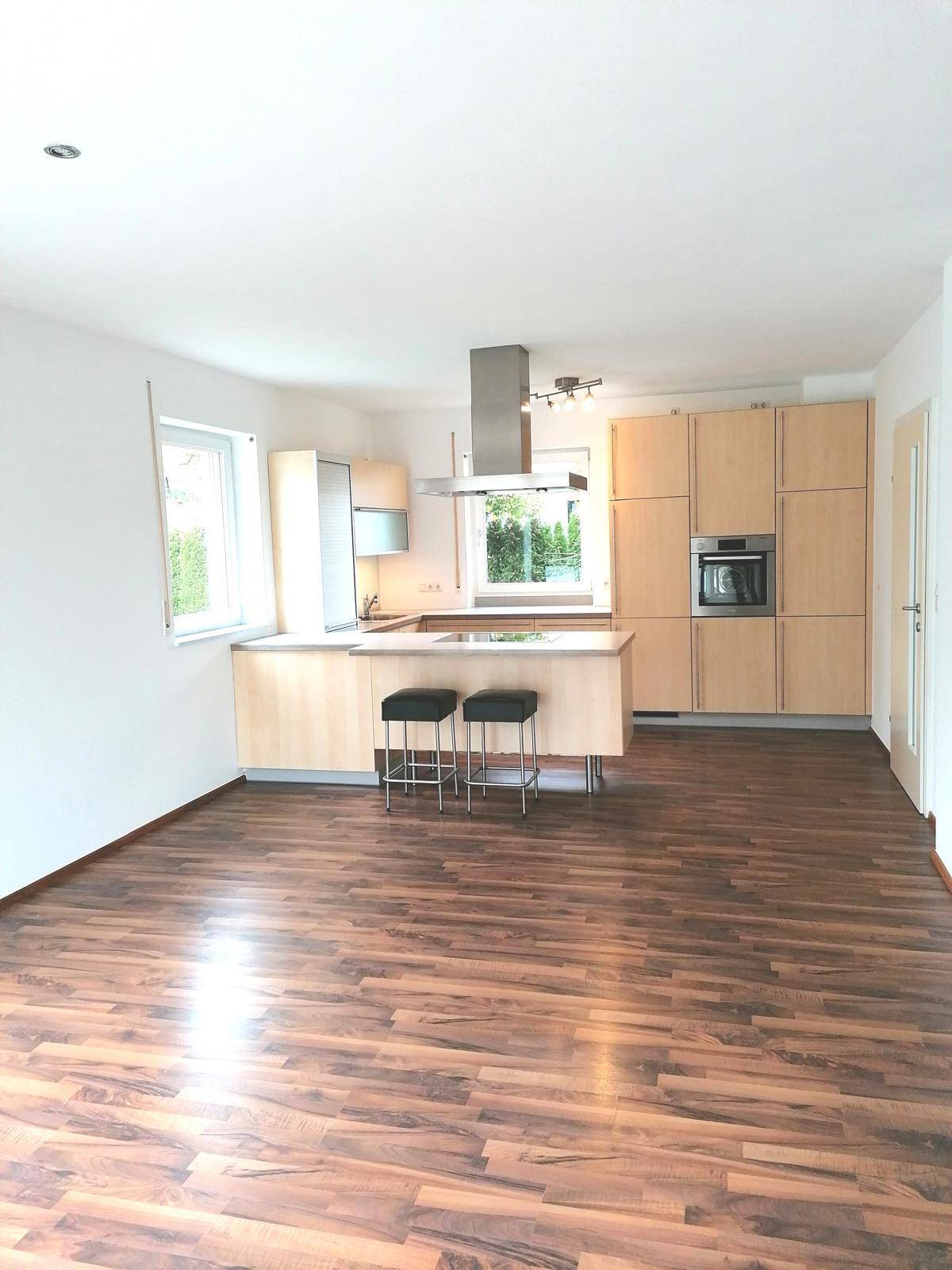 Helle, offene Küche mit Holzfronten, Kochinsel und Laminatboden in einem modernen Raum.