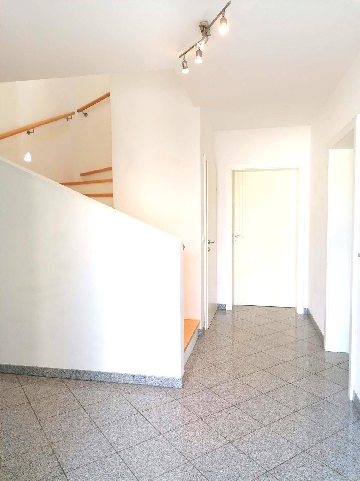 Heller Flur mit Granitfliesenboden und Holztreppe, die in die oberen Stockwerke führt.