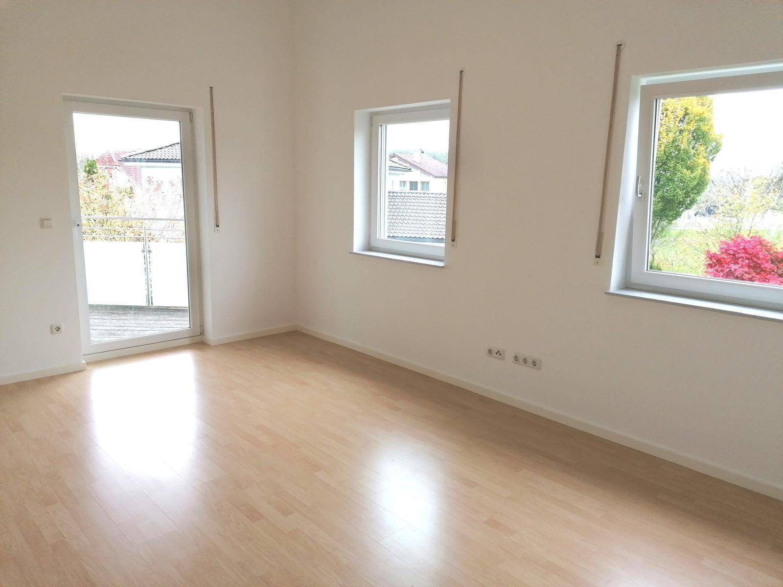 Helles Zimmer mit Laminatboden, großen Fenstern und direktem Zugang zu einem Balkon.