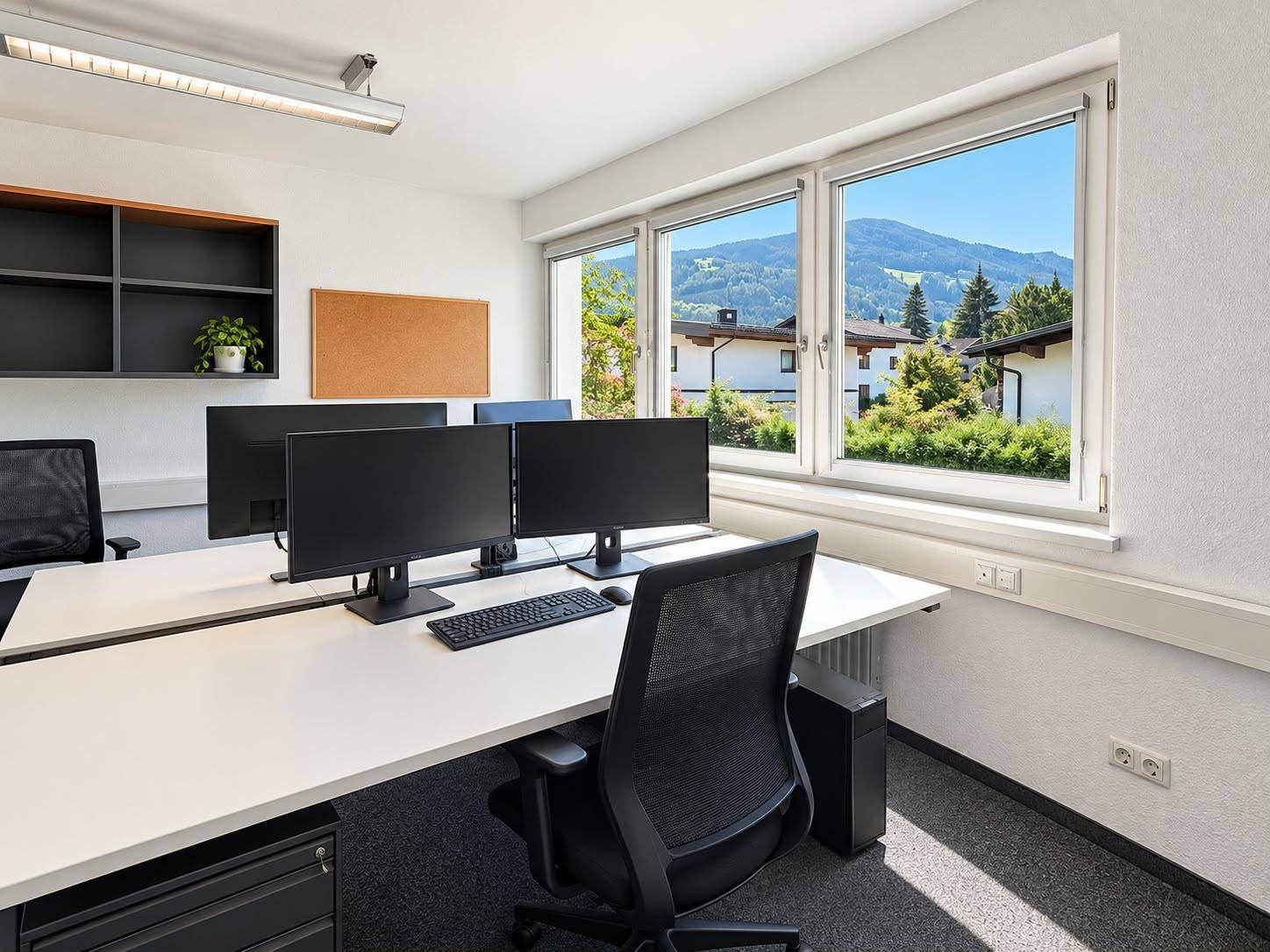 Heller Büroraum mit Arbeitsplatz, Computern und einem weiten Blick auf die Berge und grüne Landschaft.