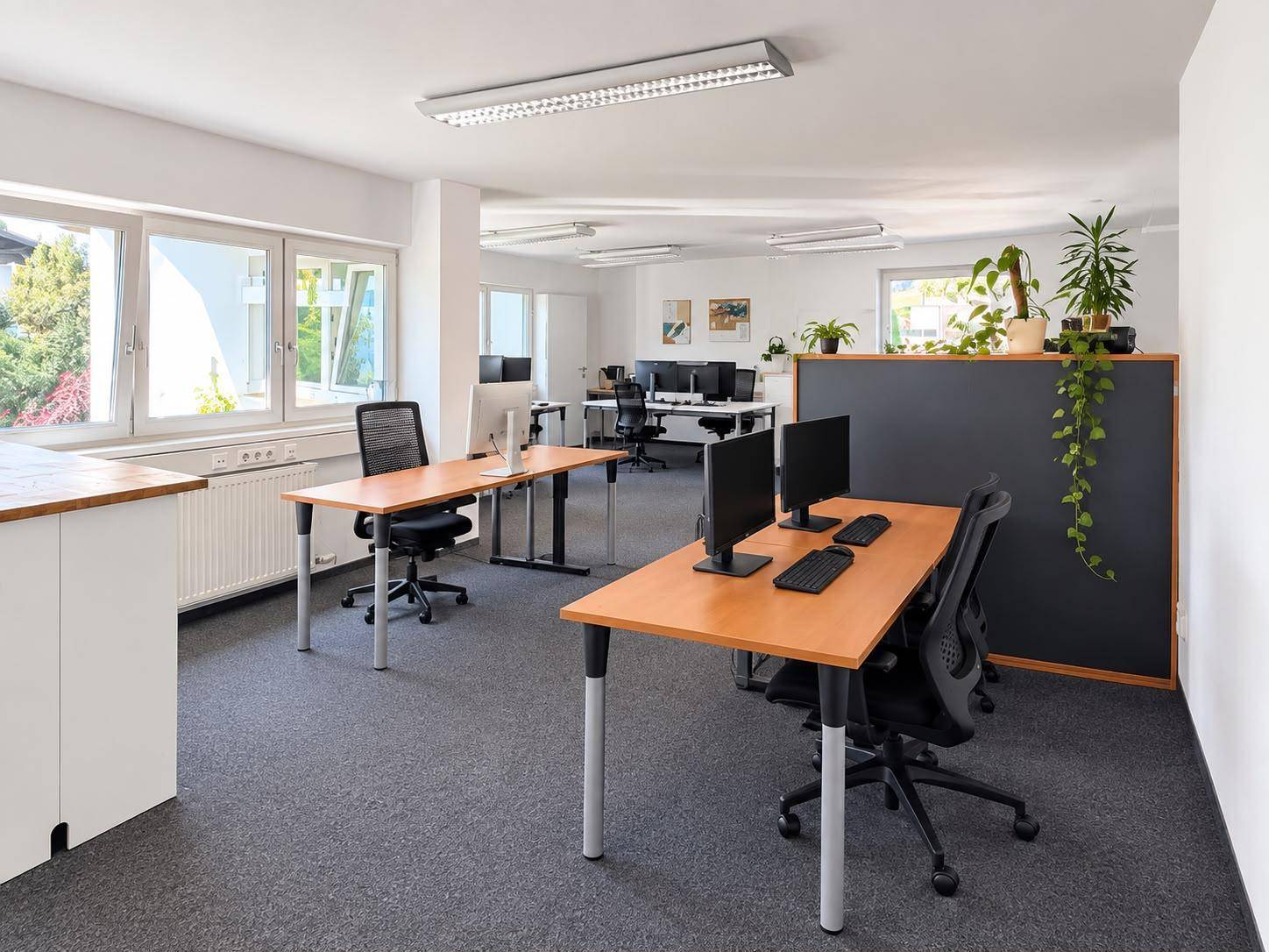 Großzügiges Großraumbüro mit mehreren Arbeitsplätzen, Computern und hellen Fenstern.