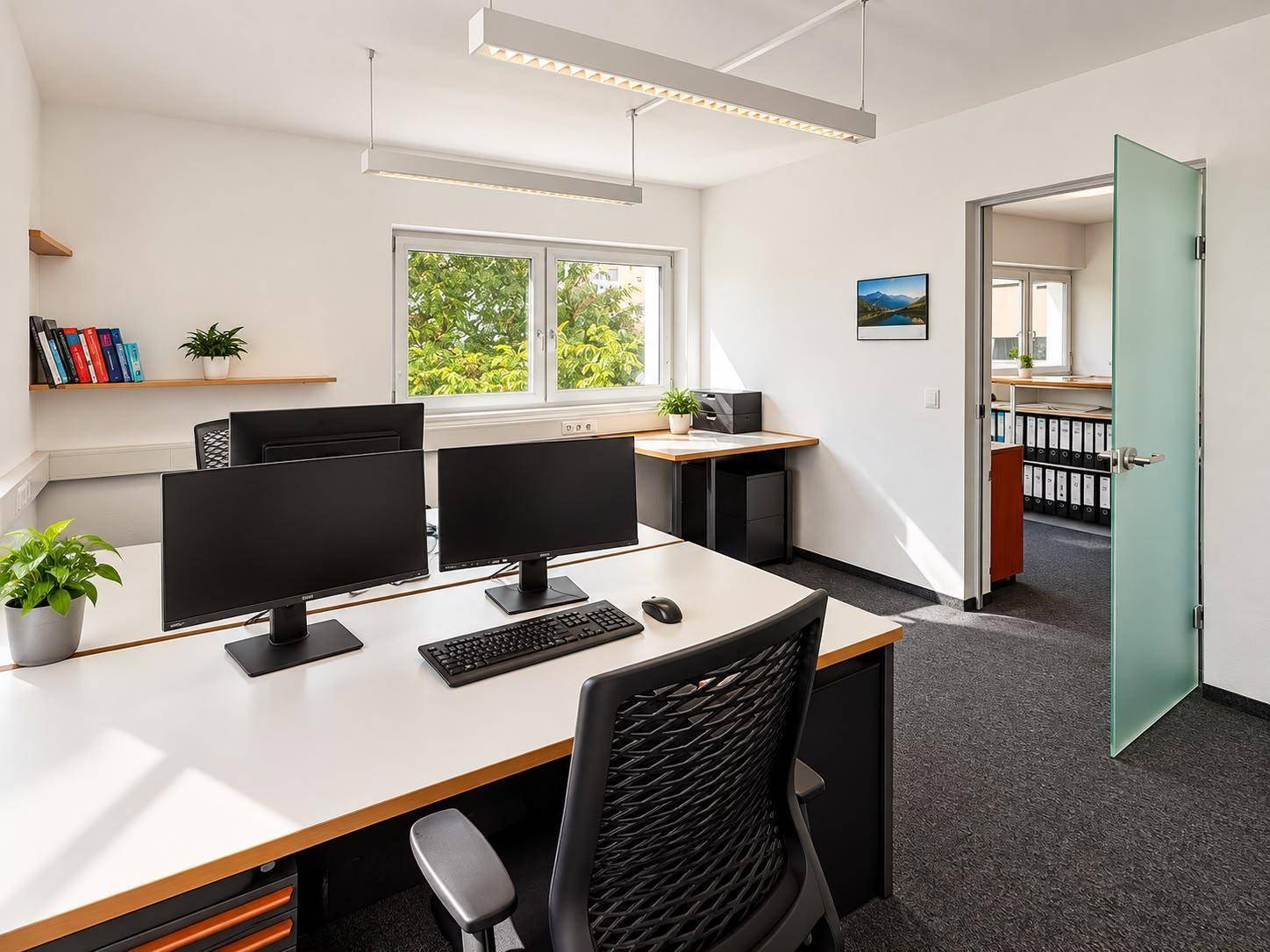 Modernes Büro mit zwei Arbeitsplätzen, Computern und einem Fenster mit Blick ins Grüne.