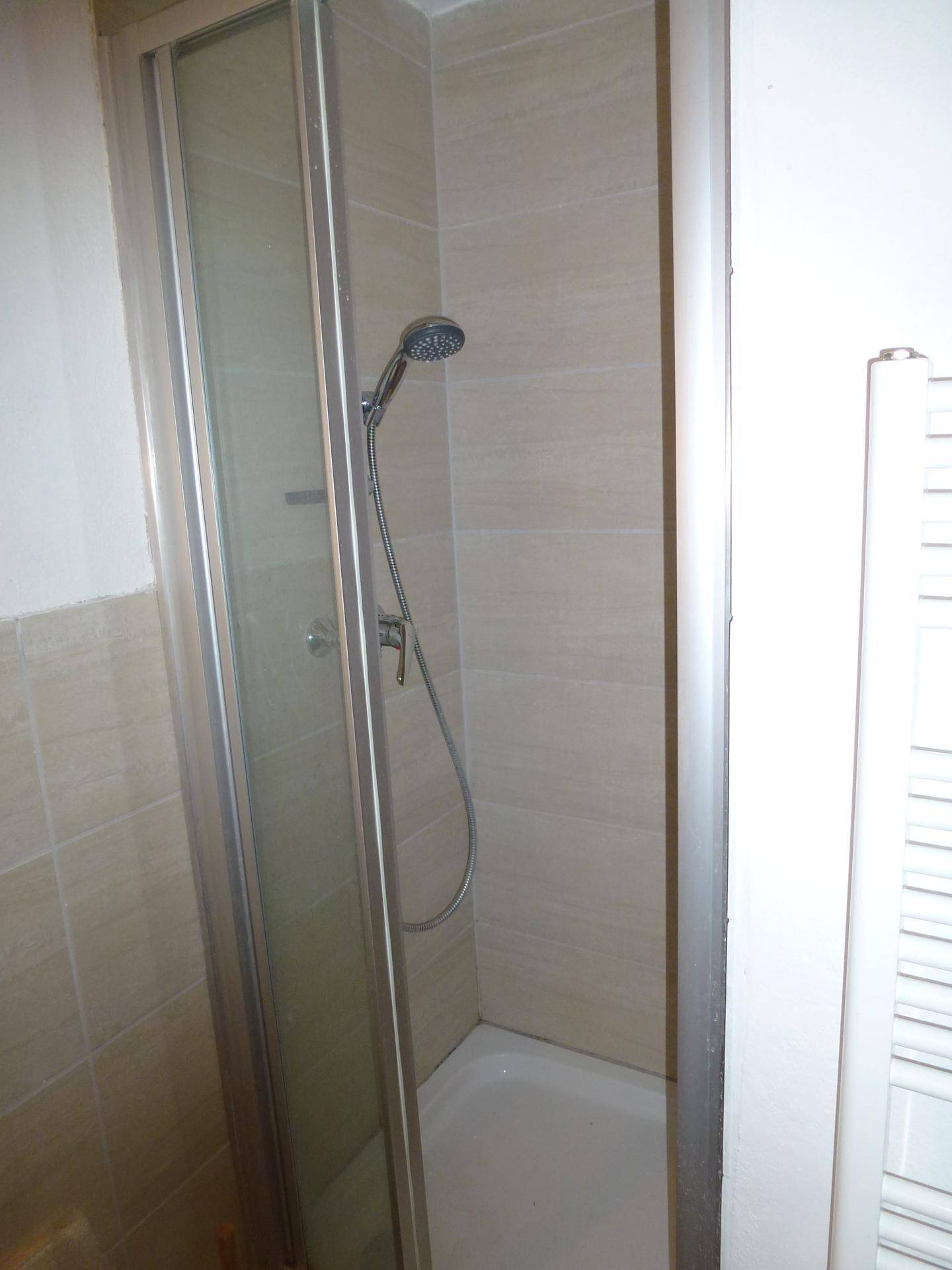 Moderne Duschkabine mit beigefarbenen Fliesen und einer Handbrause in einem gepflegten Bad.