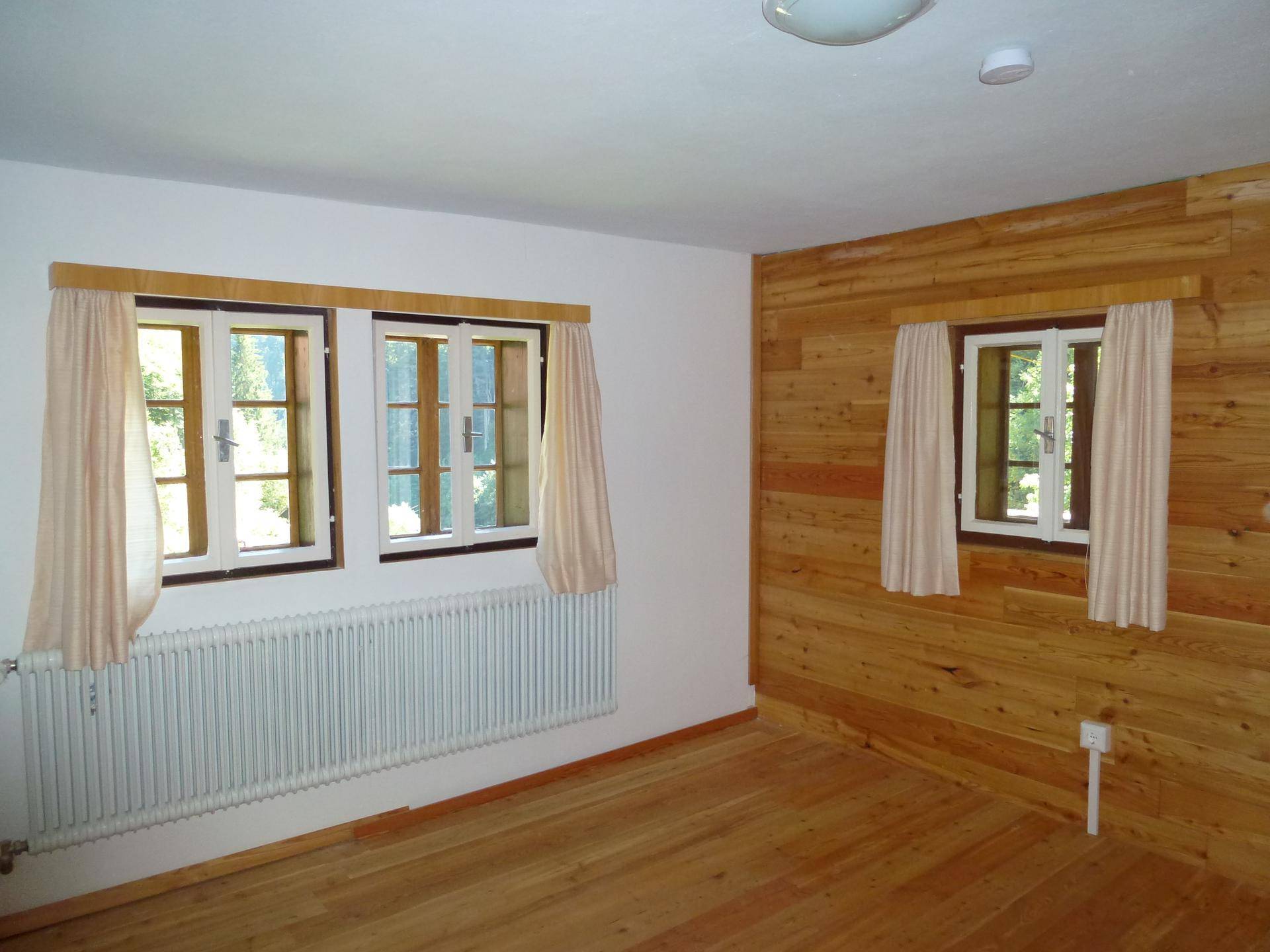 Geräumiges Zimmer mit Holzboden, Holzverkleidung und mehreren Fenstern für viel Tageslicht.
