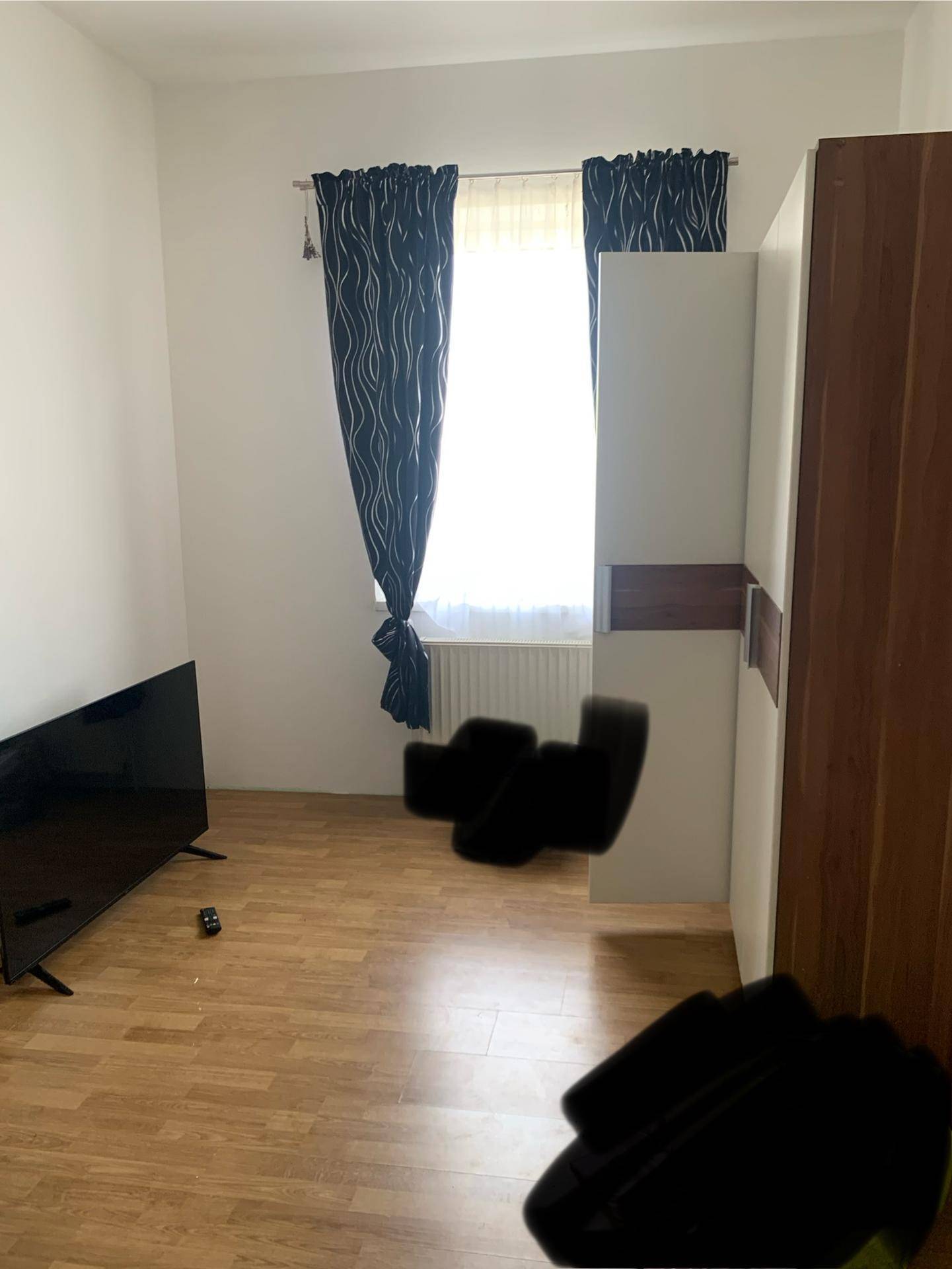 Schlafzimmer mit Laminatboden, großem Fenster und einem Kleiderschrank.