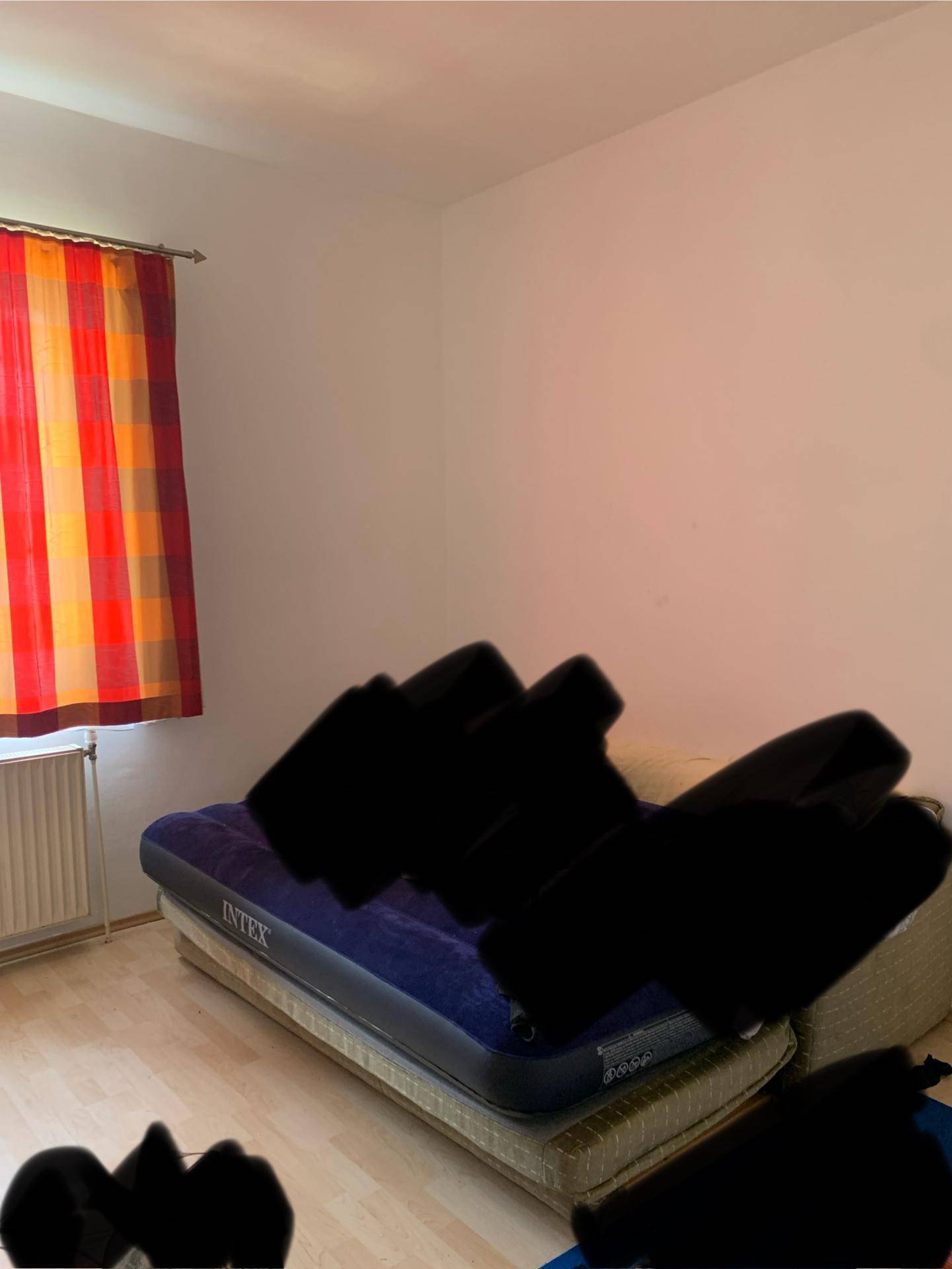 Schlafzimmer mit Laminatboden und einem Fenster mit farbigen Vorhängen.