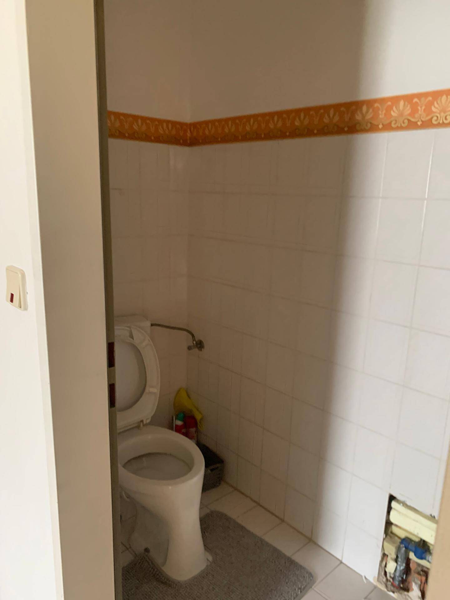 Einfache Gästetoilette mit weißen Fliesen und einem dekorativen orangefarbenen Fries.