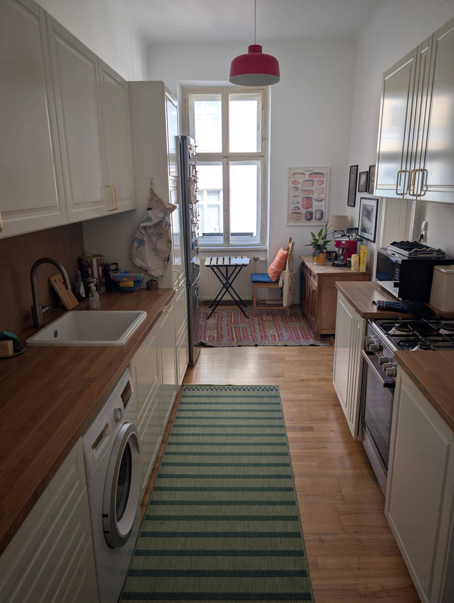 Schmale Küche mit weißen Schränken, Holzarbeitsplatten, Fenster und integrierter Waschmaschine.