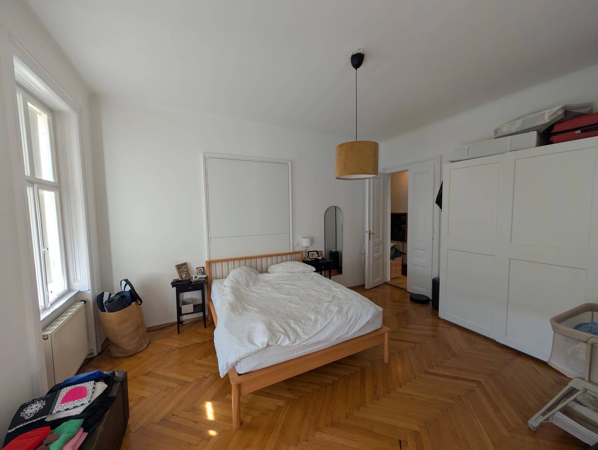Geräumiges Schlafzimmer mit Doppelbett, weißem Kleiderschrank, Parkettboden und viel Tageslicht.