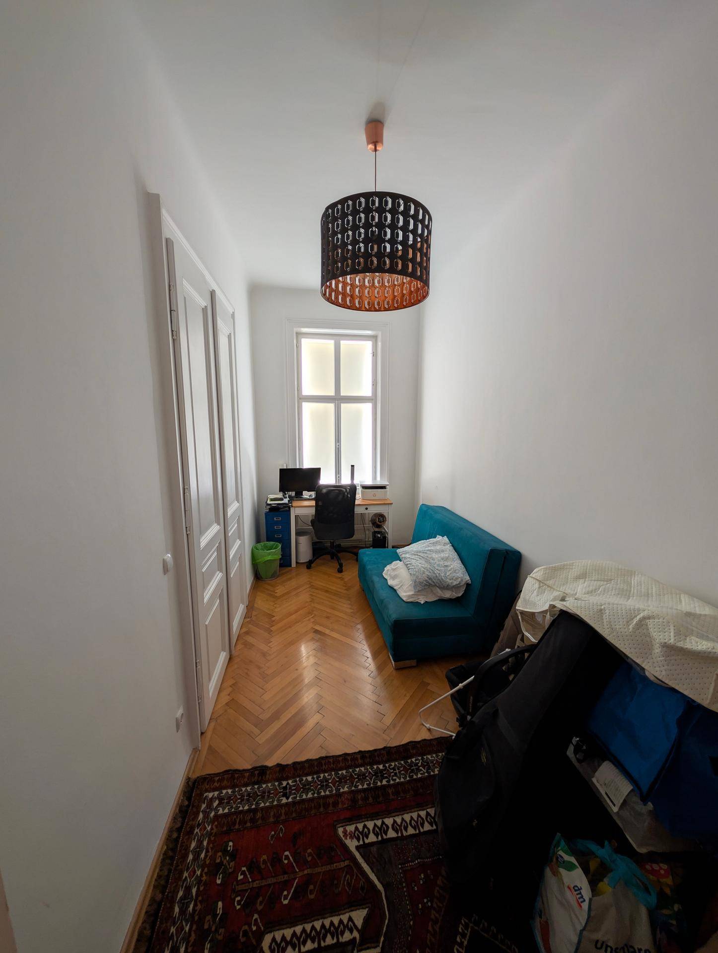 Kleines Arbeitszimmer mit Schreibtisch, Sofa und Fenster, ausgestattet mit Parkettboden.