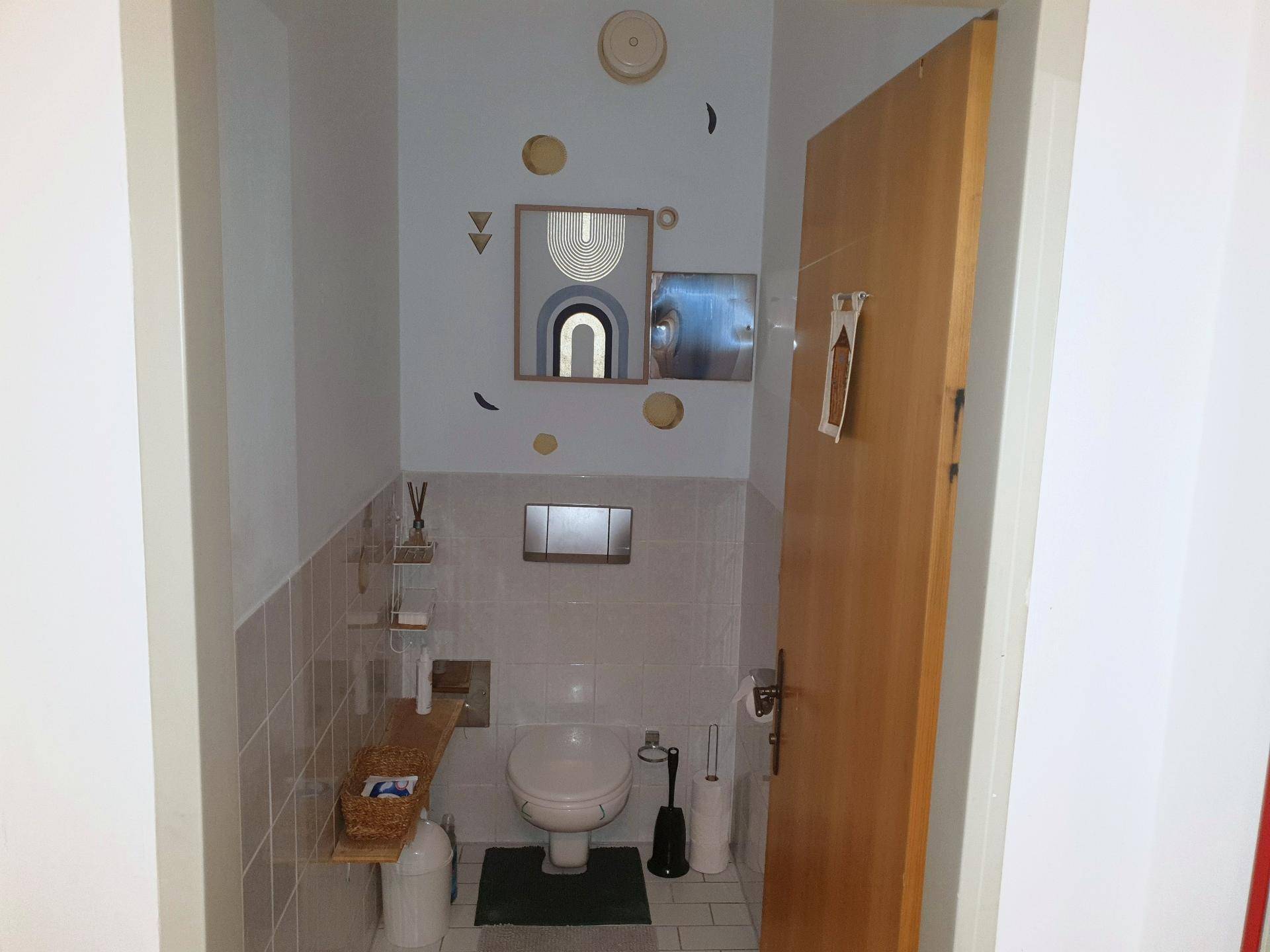 Separate Toilette mit Wand-WC, Fliesen und dekorativen Wandelementen.