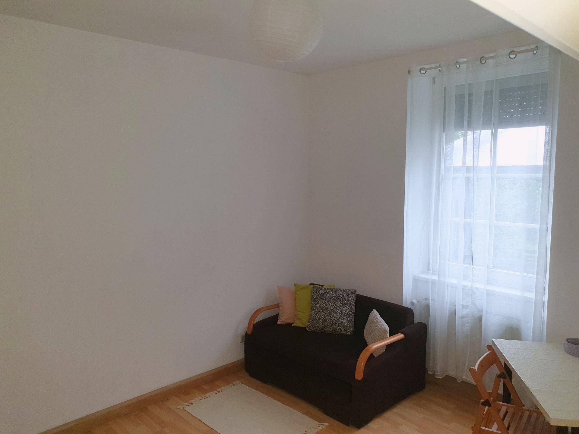 Gemütliches Schlafzimmer mit kleinem Sofa, Holzboden und Fenster mit Vorhängen.