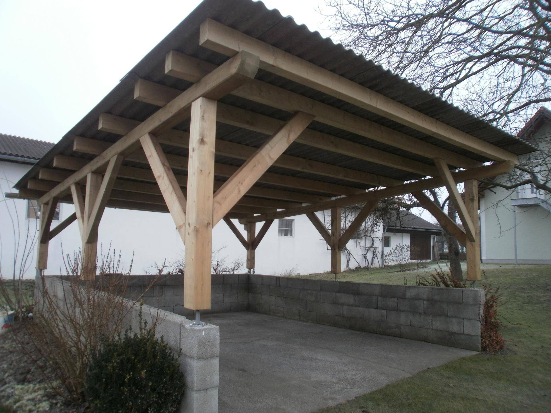 Robuster Holzcarport mit Wellblechdach und gemauerter Basis für Fahrzeuge.