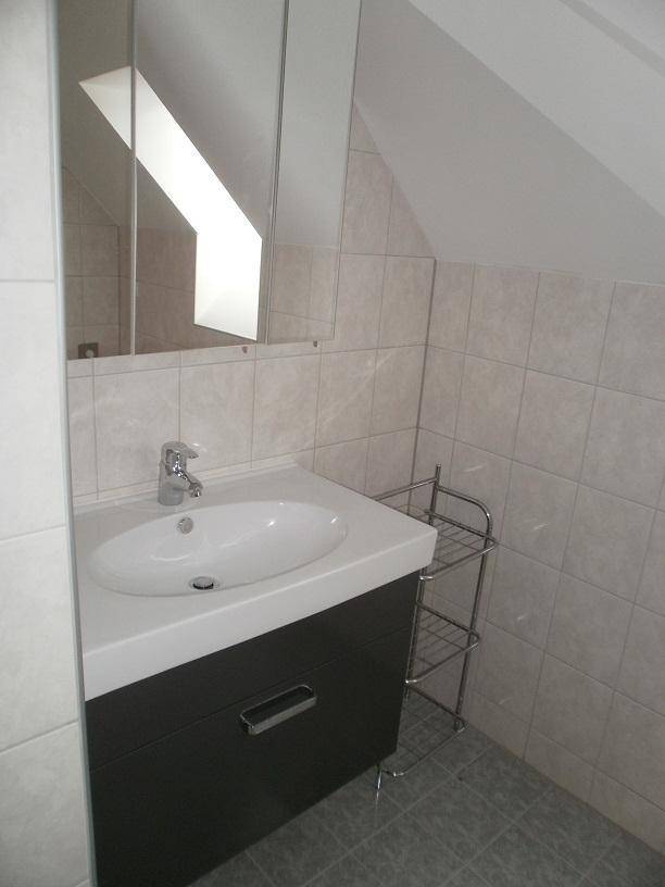 Badezimmer mit Waschbecken, Spiegelschrank, hellen Fliesen und Dachschräge.