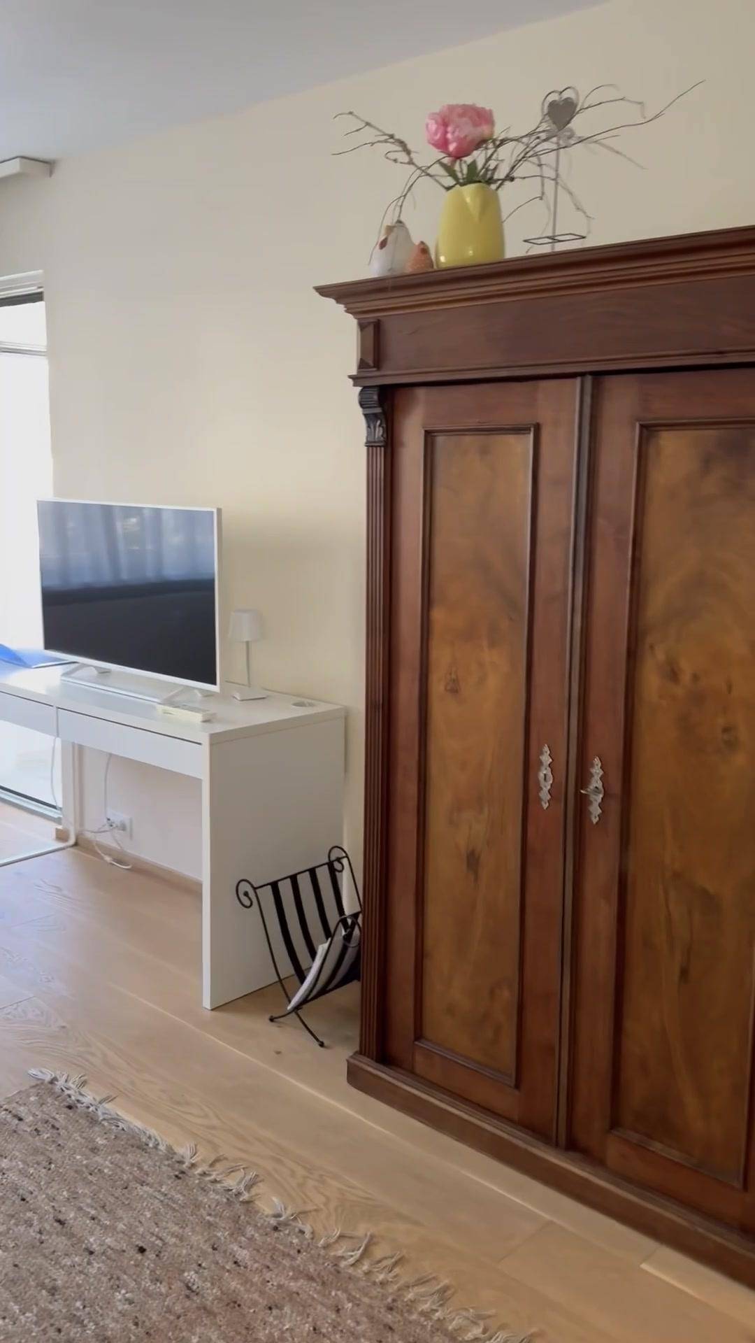 Schlafzimmer oder Arbeitsbereich mit hellem Holzboden, antikem Kleiderschrank und Schreibtisch.