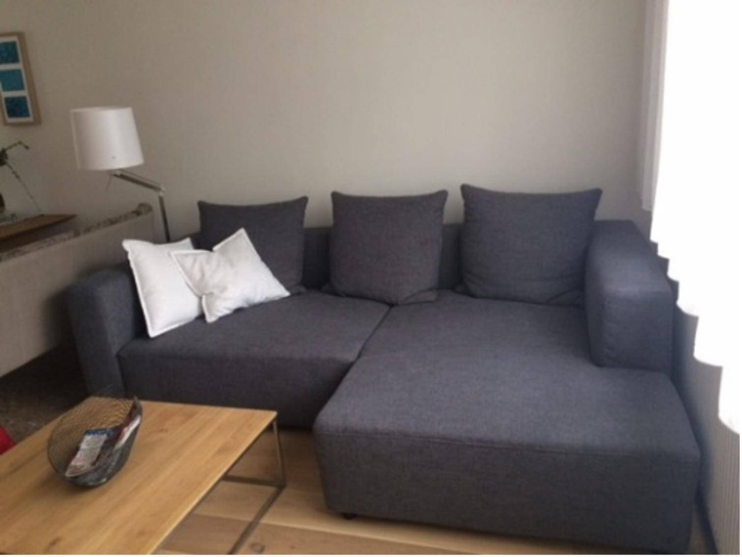 Gemütliches Wohnzimmer mit großem grauen Ecksofa, Couchtisch und heller Wandfarbe für entspannte Stunden.