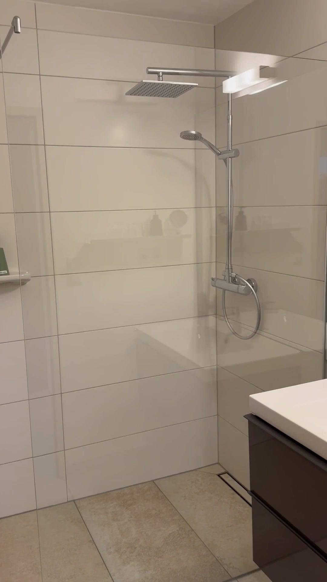 Modernes Badezimmer mit begehbarer Dusche, großen Fliesen und Regenduschkopf.