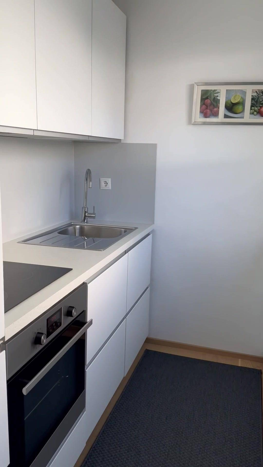 Moderne, kompakte Küche mit weißen Schränken, integriertem Backofen und Spülbecken.