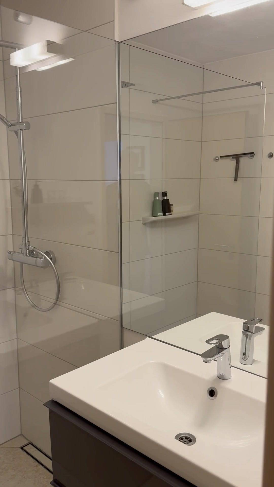 Modernes Badezimmer mit Einzelwaschbecken, großem Spiegel und begehbarer Dusche.